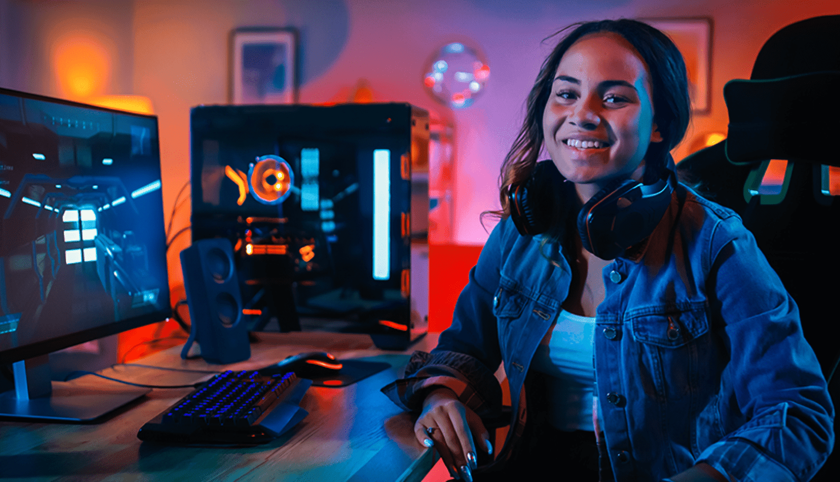 Person smiling at a gaming setup with a PC tower, monitor, and headset seated at a desk.