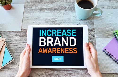 A tablet placed on top of a table displays the wording “Increase brand awareness” along with a “Start” button.
