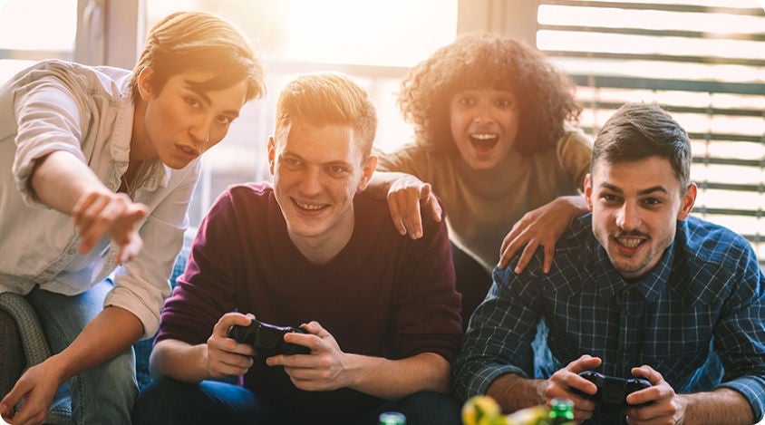 Four people gathered on a couch, excited and smiling while playing a video game with controllers.