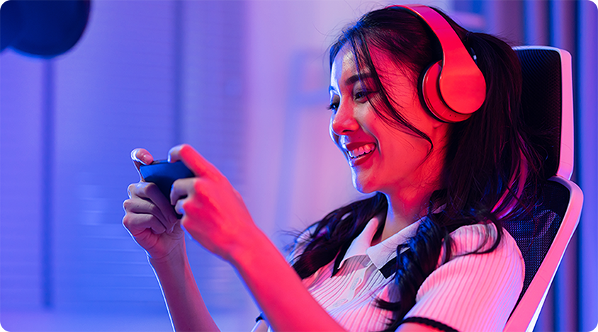 Woman smiling while playing a mobile game with headphones on in a brightly lit room with colorful neon lighting 