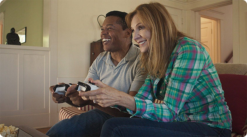Two people sitting on a couch, smiling and playing a video game together with controllers.