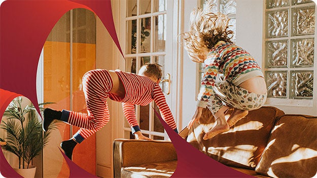 Two children in colorful pajamas joyfully jumping on a brown couch in a sunlit room, framed by artistic red shapes.