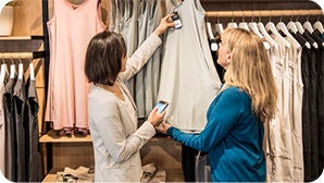 Two women looking at a piece of clothing at a retail store.