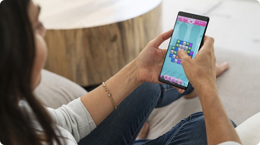 Person sitting on a couch and using their smartphone to play Candy Crush Saga.