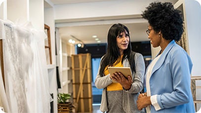 Two people standing, one person is showing the other one a tablet.