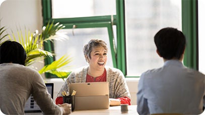 Three people sitting at a table, one person is smiling while using a tablet.