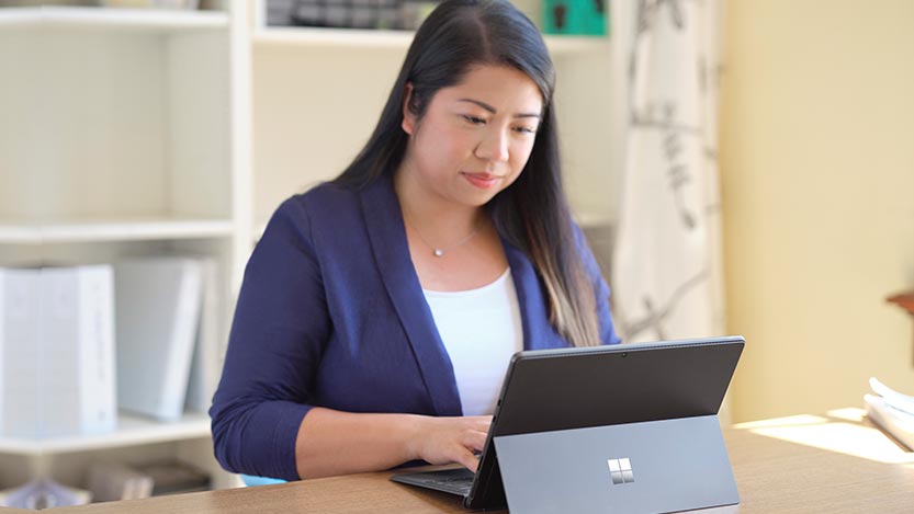  A teacher is sitting at a desk typing on a Surface Pro 8