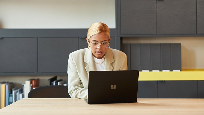 A woman sits at a table in a lounge and works on her laptop computer.