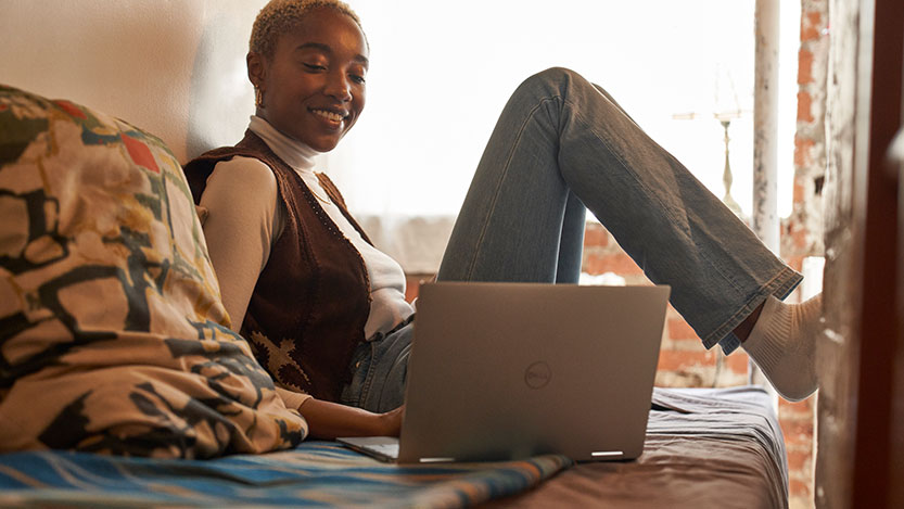 A woman sitting on a couch with her feet up works in a laptop computer.