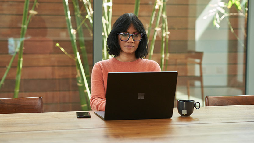 A woman facing forward sits at a desk while working on her laptop computer