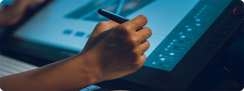 Close-up of a person using a stylus on a digital drawing tablet while working at a desk.