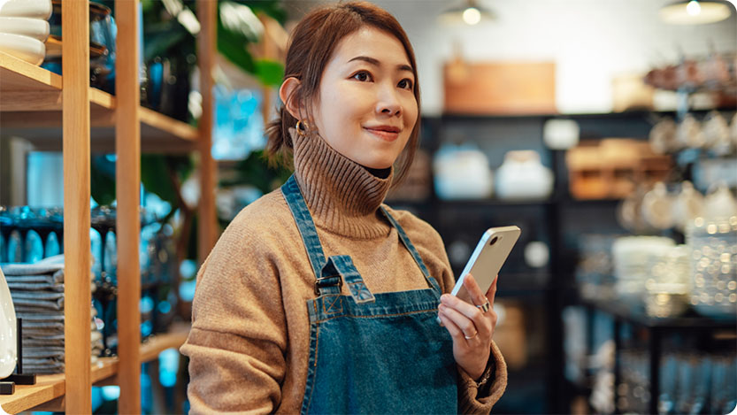 Female shop worker smiling while checking her smartphone.