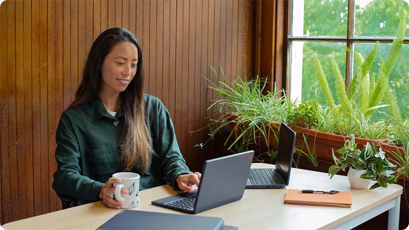 Person an einem Tisch mit einer Tasse und zwei Laptops.