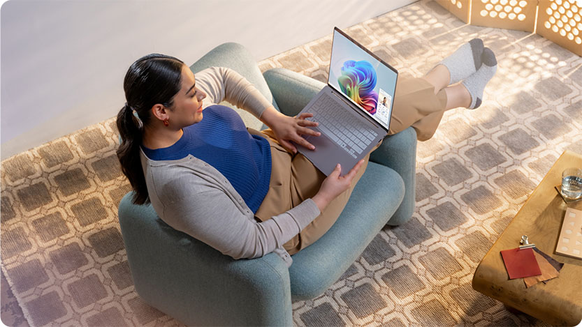 A person is sitting relaxed in an armchair indoors, holding a laptop.