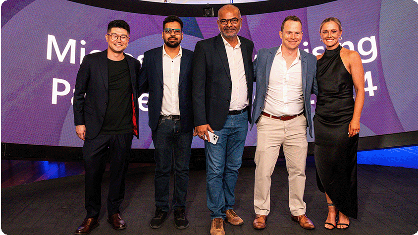 A group of five people standing together in front of a large curved screen displaying the text "Microsoft Advertising Partner 2024.