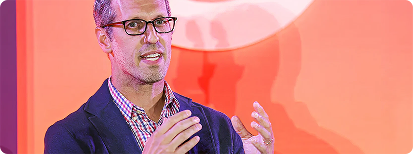Jordan Shlachter speaking onstage at Advertising Week New York, gesturing with his hands in front of stage backdrop.