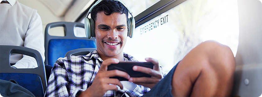 Person sitting on a bus wearing headphones and smiling while playing a game on a smartphone.