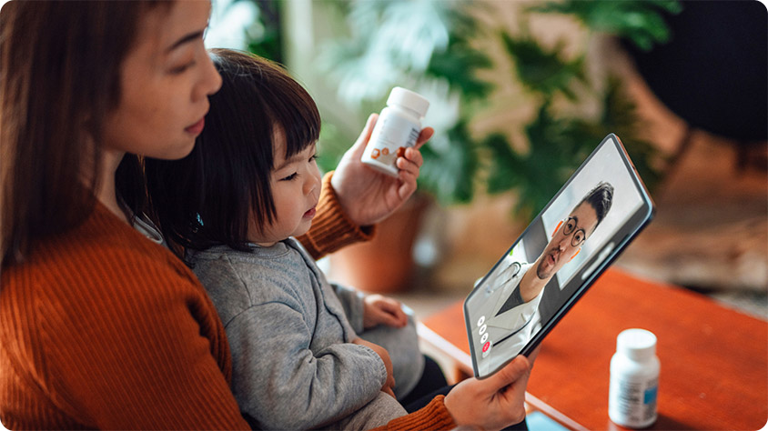 An adult person with a child using a tablet to have a video call with a doctor.